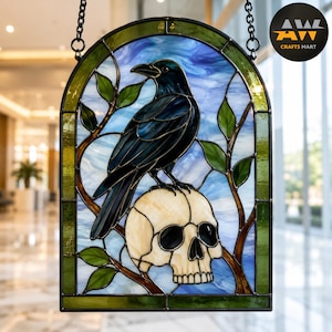 Peut inclure: Un panneau en vitrail cintré représentant un corbeau noir perché sur un crâne humain de couleur crème. Le motif comprend des branches brunes avec des feuilles vertes sur un fond de ciel bleu tourbillonnant, le tout dans un cadre en métal sombre.