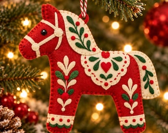May include: A red felt horse ornament featuring cream-colored felt accents, green leaf embroidery, and small red berry details. The horse has a cream-colored bridle and saddle blanket design with a central heart shape, suspended by a red and white string.