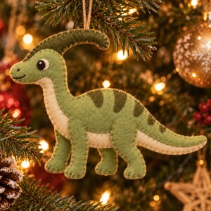 May include: A felt parasaurolophus dinosaur ornament in shades of light and dark green with a cream-colored underbelly. The dinosaur features a long crest, a stitched outline, and a small twine loop at the top for hanging on a tree.