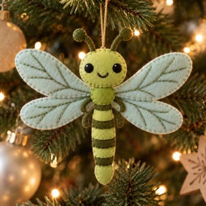 May include: A felt dragonfly ornament featuring a light green head and body with dark green horizontal stripes. The insect has large, pale mint-colored wings with dark green stitched vein details, two antennae with rounded tips, and black eyes.