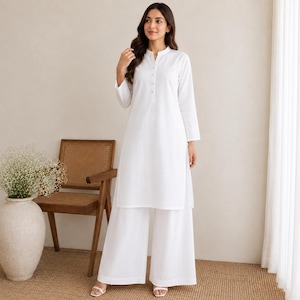 May include: A solid white long-sleeved tunic featuring a mandarin collar and a partial button-down placket, paired with matching wide-leg trousers. The ensemble is crafted from a plain, opaque fabric, creating a clean and uniform monochromatic look.