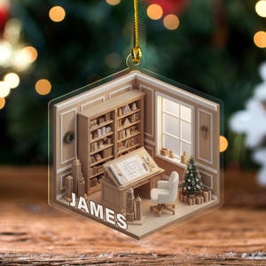 May include: A hexagonal acrylic ornament featuring a 3D-style illustration of an office interior with light wood bookshelves, a drafting desk with blueprints, a white chair, and a small Christmas tree. The name JAMES is printed in white.