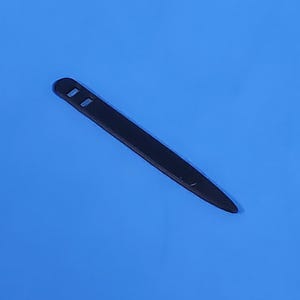 May include: A slender, matte black plastic collar stay with a pointed tip and a rounded end featuring two small rectangular cutouts. The object is positioned diagonally against a solid, vibrant blue background, showcasing its smooth, flat surface.
