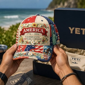 May include: A baseball cap featuring a patchwork design of American flag motifs, floral patterns, and the Statue of Liberty. The front panel displays the text AMERICA 1776-2026 CELEBRATING 250 YEARS OF FREEDOM in red and black lettering.
