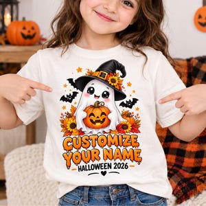 May include: A cream-coloured t-shirt featuring a graphic of a white ghost wearing a black witch hat with sunflowers, holding a jack-o'-lantern. The design includes bats, autumn leaves, and the text "CUSTOMIZE YOUR NAME HALLOWEEN 2026".