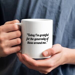 Può includere: Una tazza in ceramica bianca con il testo stampato in nero: "Today I'm grateful for the generosity of those around me." La tazza presenta un corpo cilindrico liscio e un manico curvo sul lato, progettata per contenere bevande calde o fredde.