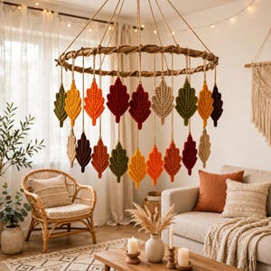 May include: A circular wooden branch mobile featuring multiple hanging macrame leaves in autumn colors including deep red, burnt orange, mustard yellow, olive green, and cream. The leaves are suspended by thin twine from the central branch ring.