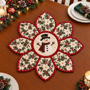 Könnte beinhalten: Ein gestepptes Stoff-Platzset in Form einer Blume mit acht Blütenblättern. In der Mitte befindet sich ein Schneemann mit schwarzem Zylinder und rot-grün gestreiftem Schal. Die Blütenblätter zeigen ein Muster aus weißen Weihnachtssternen und Stechpalmen.
