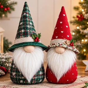 May include: Two plush gnome figurines with long white beards and tall pointed hats. The left gnome wears a green plaid hat with snowflakes, while the right gnome has a red hat with white hearts and a floral brim, both accented with holly berries.
