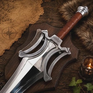 May include: A silver-toned sword with a brown leather-wrapped handle and a metallic pommel. The crossguard features an intricate, curved design with engraved markings. The blade is polished and reflective, tapering to a point at the bottom edge.