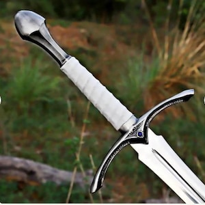 May include: A silver-toned metal sword featuring a white wrapped handle, a rounded pommel, and a crossguard with curved quillons. The center of the crossguard displays a small, circular blue gemstone set into the polished metal surface.