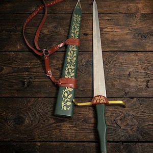 Peut inclure: Une dague en métal longue et pointue avec un manche vert, une garde en laiton et un pommeau en laiton. Elle comprend un fourreau vert assorti orné de motifs de feuilles de chêne dorées et un système de lanières en cuir marron avec des anneaux et des boucles en métal.