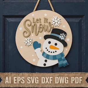 Puede incluir: Un letrero de puerta circular de madera con un muñeco de nieve con sombrero negro y bufanda azul, el texto Let It Snow y copos de nieve blancos. Tiene una cuerda para colgar. Una pancarta de arpillera en la parte inferior muestra AI EPS SVG DXF DWG PDF.
