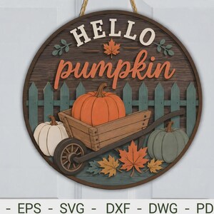 Peut inclure: Une plaque murale ronde en bois avec le texte HELLO pumpkin en blanc et orange. Le motif représente une brouette en bois contenant une citrouille orange, entourée d'une citrouille blanche et d'une verte, devant une clôture verte avec des feuilles.