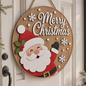 Peut inclure: Une plaque de porte ronde en bois avec une illustration superposée du Père Noël portant un bonnet rouge, une barbe blanche et des gants noirs. Le texte blanc Merry Christmas est accompagné de flocons de neige et de points sur fond bois.