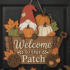 May include: A wooden wall hanging sign featuring a gnome wearing a red hat, sitting in a wagon filled with orange, green, and white pumpkins and autumn leaves. The sign displays the text Welcome to Our Patch in white and brown lettering.