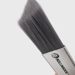 May include: A paint brush with long, dark gray synthetic bristles arranged in an angled, tapered shape. The metal ferrule is silver and features the black text ROLLINGDOG with a circular logo icon. The handle is black with a textured grip area.