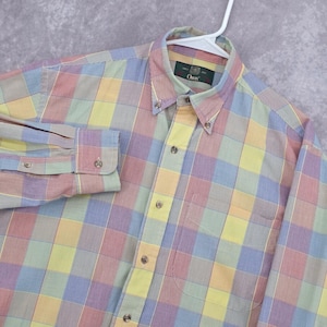 Pode incluir: Uma camisa de manga comprida com botões e um padrão xadrez multicolorido em tons de amarelo, azul, vermelho e verde. A camisa tem uma gola abotoada, uma carcela frontal com botões e um bolso no peito. A etiqueta interior diz Orvis.