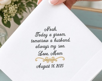 Peut inclure: Un mouchoir carré blanc avec une broderie noire portant le texte : Noah, Today a groom, tomorrow a husband, always my son. Love, Mom, accompagné d'une fioriture dorée et de la date du 16 août 2025, centrés sur le tissu.