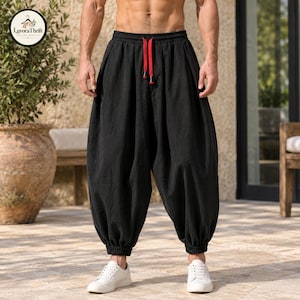 May include: Black loose-fitting trousers with a gathered elastic waistband and cuffs. The pants feature a bright red drawstring with dark tips at the center front. The fabric has a textured appearance and a relaxed, wide-leg silhouette.
