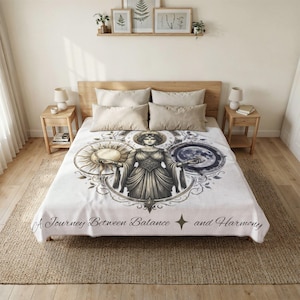 Könnte beinhalten: Eine weiße Tagesdecke mit einer zentralen Illustration einer Figur zwischen Sonne und Mond. Das Design umfasst detaillierte Linienführung und den Text A Journey Between Balance and Harmony, der unten in einer dunklen Schreibschrift gedruckt ist.