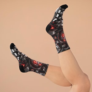 May include: A pair of crew socks featuring a dark, mechanical-inspired print with metallic gray and black panels, intricate piping details, and glowing red circular accents throughout the fabric, finished with solid black heels and toe sections.