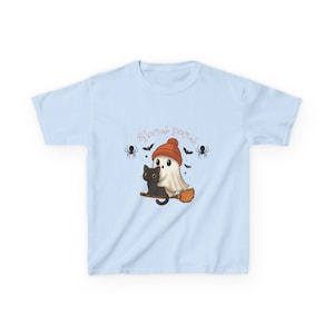 Könnte beinhalten: Ein hellblaues T-Shirt mit einer Grafik eines weißen Geistes mit orangefarbener Mütze und einer schwarzen Katze, die zusammen auf einem Besenstiel sitzen. Der Text Hocus Pocus steht über den Figuren, umgeben von kleinen schwarzen Spinnen und Fledermäusen.