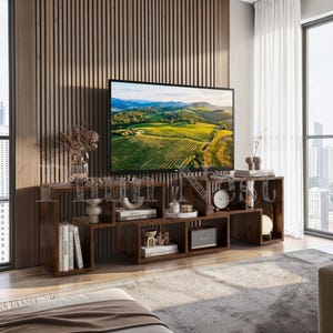 May include: A dark brown wooden media console with an asymmetrical, multi-level open shelving design. The unit features various rectangular compartments holding books, a small round clock, a speaker, and decorative ceramic objects.