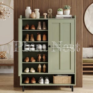 May include: A sage green shoe cabinet with one open door and one closed door, featuring six interior shelves filled with various pairs of shoes, a bottom open shelf with a woven basket, and a top surface holding decorative vases and small potted plants.