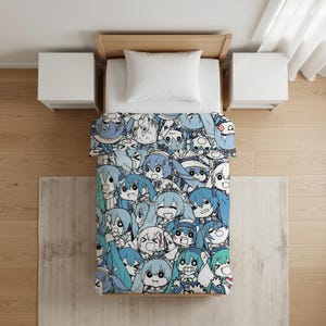 Op de afbeelding: Een eenpersoonsbed met een dekbedovertrek met een dicht, herhalend patroon van blauwharige anime-stijl personages met diverse chibi-uitdrukkingen. Het bed bevat een effen wit kussen en een lichthouten frame, gezien vanuit vogelperspectief.