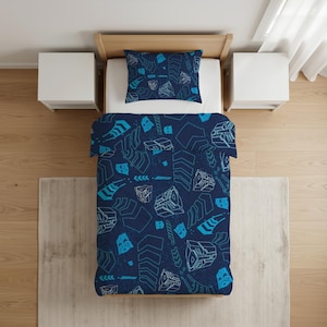 May include: A single bed featuring a dark blue duvet cover and a matching pillowcase. The bedding set is decorated with a repeating pattern of light blue and white geometric shapes and stylised robot face icons scattered across the fabric surface.