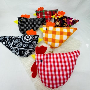 May include: A collection of six stuffed fabric chicken ornaments featuring various patterns including red and white gingham, black and white paisley, black polka dots, red plaid, and a floral print, each with a bright orange or red felt comb.