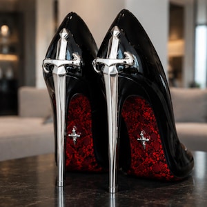 May include: A pair of black patent leather high-heeled pumps featuring a metallic silver sword-shaped stiletto heel. The soles are a vibrant red with a black lace-like pattern and a small silver cross emblem embedded in the center of each sole.