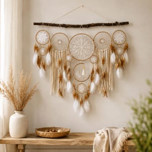 May include: A large wall hanging featuring five circular crochet dreamcatchers and a central crescent moon shape suspended from a dark wooden branch. The piece is decorated with long cream-coloured fringe, white and brown feathers, and beads.