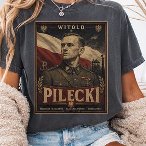 May include: A charcoal gray short-sleeve t-shirt featuring a graphic print of Witold Pilecki in a military uniform. The design includes the Polish flag, the text WITOLD PILECKI, and the phrases VOLUNTEER TO AUSCHWITZ, RESISTANCE FIGHTER, and EXECUTED 1948.