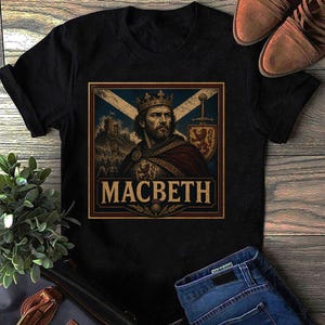 Peut inclure: Un t-shirt noir à manches courtes avec une impression graphique représentant un roi barbu portant une couronne et une cape. Le motif comprend un château, une épée, un bouclier avec un emblème de lion et le texte MACBETH centré dans un cadre.