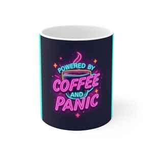 Puede incluir: Una taza de cerámica de color oscuro con un gráfico estilo neón de una taza de café con vapor. El texto "POWERED BY COFFEE AND PANIC" aparece en letras de neón rosa brillante y azul claro, rodeado de pequeños acentos de estrellas brillantes.
