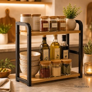 May include: A two-tier spice rack with a black metal frame and light wood shelves. The top shelf holds three white jars labeled Salt, Sugar, and Paprika, plus three glass jars with wood lids labeled Paprika, Oregano, and Cinnamon.