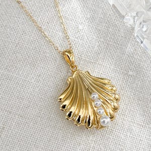 Op de afbeelding: Een gouden ketting met een schelp hanger en parel accenten. De schelp is gedetailleerd met ribbels en heeft een gladde, gepolijste afwerking.