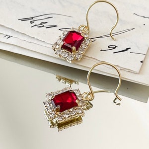 May include: A pair of gold earrings with a red gemstone surrounded by clear rhinestones.