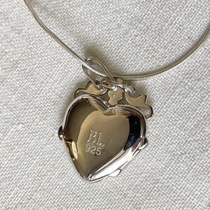 May include: A silver heart-shaped locket necklace with a chain. The locket has a small key charm and the inscription "BL 925" on the back.
