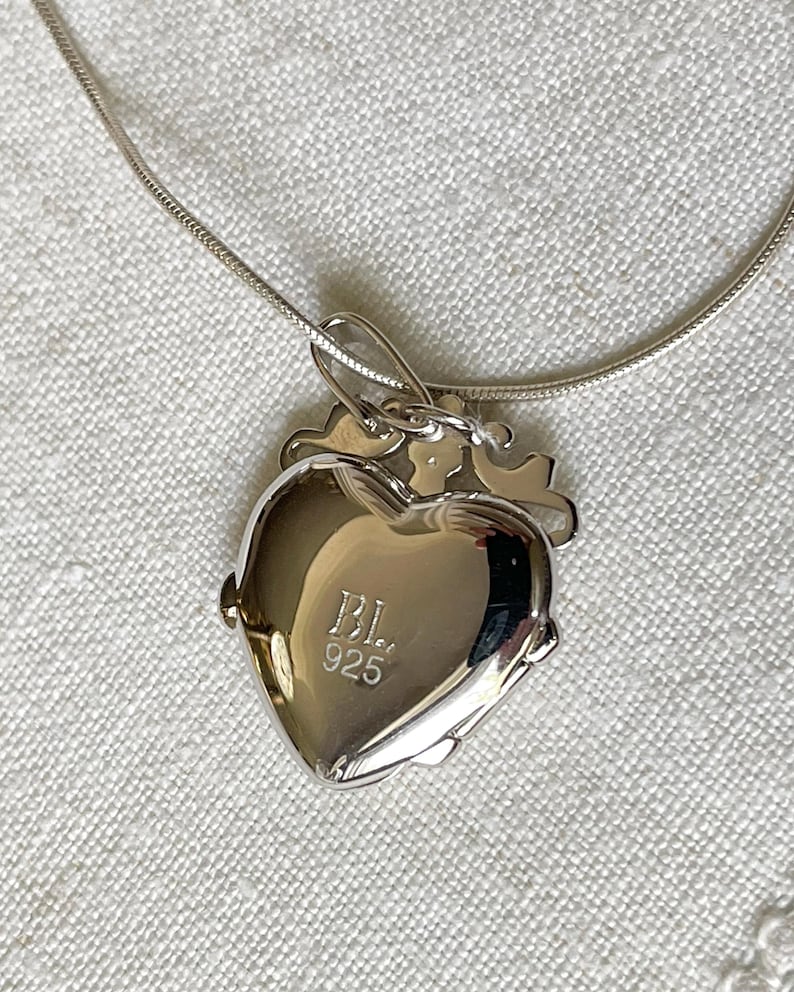 May include: A silver heart-shaped locket necklace with a chain. The locket has a small key charm and the inscription "BL 925" on the back.