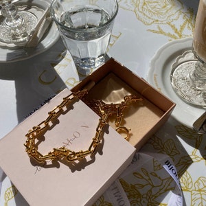 K&ouml;nnte beinhalten: Eine wei&szlig;e Keramik-Tasse mit schwarzem Henkel und dem Text "But First, Coffee" in schwarzer, fetter Schrift. Die Tasse steht auf einer wei&szlig;en Oberfl&auml;che.
