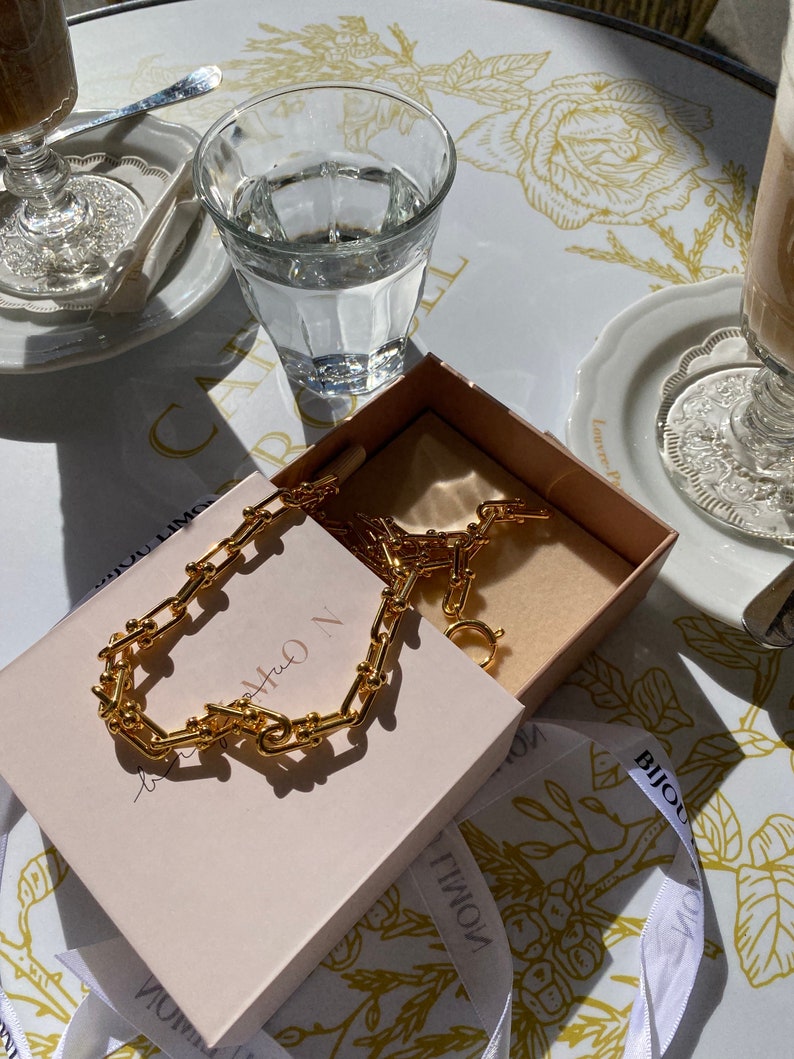 K&ouml;nnte beinhalten: Eine wei&szlig;e Keramik-Tasse mit schwarzem Henkel und dem Text "But First, Coffee" in schwarzer, fetter Schrift. Die Tasse steht auf einer wei&szlig;en Oberfl&auml;che.