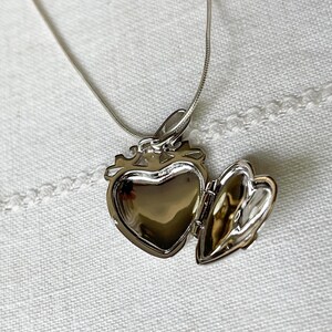 May include: A silver heart-shaped locket necklace with a hinged lid open, revealing the empty interior. The chain is a delicate silver snake chain.