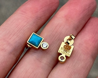 May include: A pair of gold-toned stud earrings featuring a square turquoise stone and a small round clear stone. The back of the earring is stamped with 925 and the text BIJOU LIMON. The design includes a post and a secure butterfly earring back.