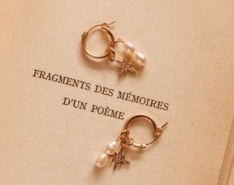 May include: Gold hoop earrings with pearl and star charms. The earrings feature a small hoop design with a dangling cluster of two pearls and a star-shaped charm with small, sparkling embellishments. The earrings are displayed on a vintage book page.