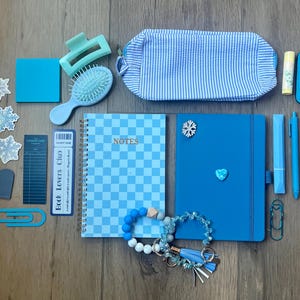 Può includere: Una collezione di articoli di cancelleria e accessori blu che include un quaderno a spirale a scacchi, un diario blu tinta unita, un astuccio a righe, un fermaglio per capelli, una spazzola, adesivi a fiocco di neve, balsamo labbra, portachiavi e braccialetti.
