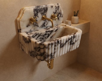 May include: A wall-mounted marble sink featuring a white and dark grey veined pattern with a fluted exterior design. The sink includes a gold-toned faucet and two matching gold-toned cross-handle knobs mounted on the integrated marble backsplash.