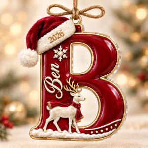 May include: A glossy red letter B Christmas ornament featuring a white reindeer wearing a red scarf, a white snowflake, and the name Ben. The letter is topped with a plush red and white Santa hat and the year 2026, hanging from a jute twine bow.